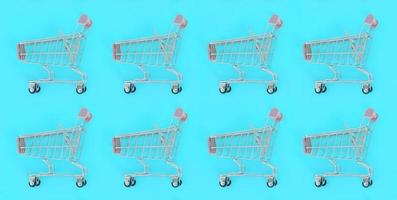 Shopping addiction, shopping lover or shopaholic concept. Many small empty shopping carts perform a pattern on a pastel colored paper background. Flat lay composition, top view photo