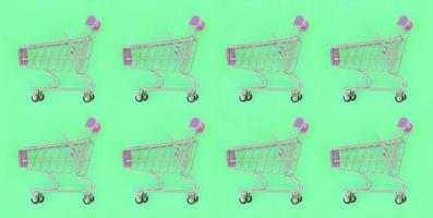 Shopping addiction, shopping lover or shopaholic concept. Many small empty shopping carts perform a pattern on a pastel colored paper background. Flat lay composition, top view photo