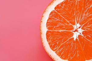 Top view of a one grapefruit slice on bright background in light pink color. A saturated citrus texture image photo