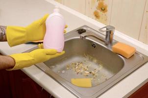 Cleaner shows liquid cleanser detergent bottle at dirty kitchen sink with food particles before the cleaning photo