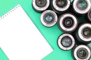 Several photographic lenses and white notebook lie on a bright turquoise background. Copy space photo