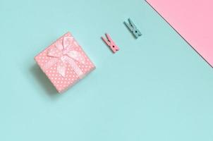 una pequeña caja de regalo rosa y dos clavijas se encuentran en el fondo de textura de papel de colores azul pastel y rosa de moda en un concepto mínimo foto