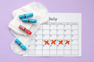 Menstrual pads and tampons on menstruation period calendar flat lay on lilac background photo