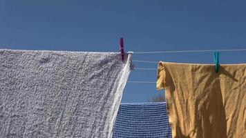 Farbige Handtücher, die sich an einem sonnigen Tag mit blauem Himmel auf einer Wäscheleine im Wind bewegen video