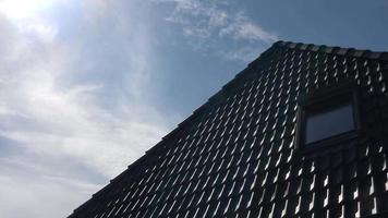 Timelape of a roof window in velux style with black roof tiles - clouds passing by in a blue sky video