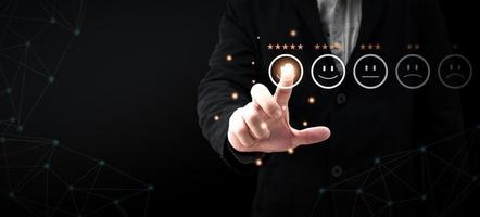 a businessman in a suit are touching the virtual screen on the happy Smiley face icon to give satisfaction in service.rating very impressed.Customer service and Satisfaction concept photo