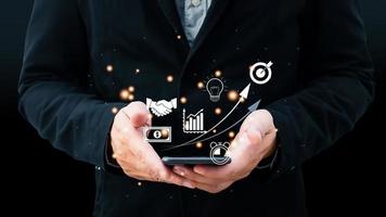Businessman holding a smartphone with icon business and network connection on modern virtual interface from digital smartphone.Use technology to plan strategy to success goals and growth. photo