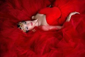 Beautiful woman in long red dress and in royal crown indoor photo