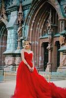 bella mujer con vestido rojo largo y corona real casi catedral católica foto