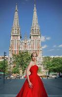 Beautiful woman in long red dress and in royal crown nearly catholic cathedral photo