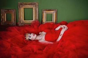 Beautiful woman in long red dress and in royal crown by the golden picture frames photo