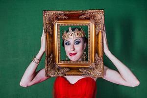 Beautiful woman in long red dress and in royal crown by the golden picture frames photo