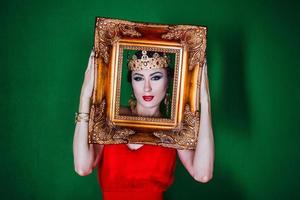 Beautiful woman in long red dress and in royal crown by the golden picture frames photo