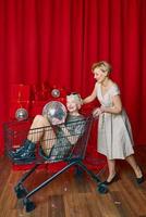 Mature woman rolling stylish senior woman in sunglasses and silver dress the supermarket cart at the party. party, disco, celebration, senior age concept photo