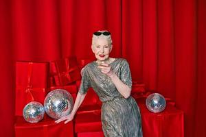 Senior stylish elegant woman with glass of sparkling wine on red background. Party, fashion, celebration, anti age concept photo