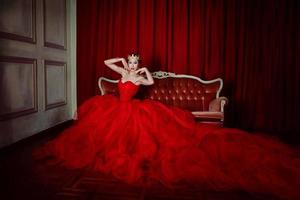 Beautiful woman in long red dress and in royal crown indoor photo