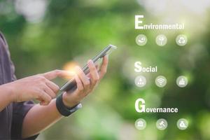 Hand holding Phone ESG icon concept in the hand for environmental, social, and governance in sustainable and ethical business on the Network connection on a green background. photo