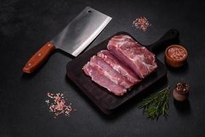 Fresh piece of raw pork with spices, salt and herbs on a wooden cutting board photo