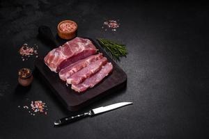 pieza fresca de cerdo crudo con especias, sal y hierbas en una tabla de cortar de madera foto