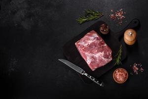 Fresh piece of raw pork with spices, salt and herbs on a wooden cutting board photo