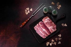 Fresh piece of raw pork with spices, salt and herbs on a wooden cutting board photo