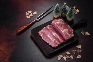 pieza fresca de cerdo crudo con especias, sal y hierbas en una tabla de cortar de madera foto