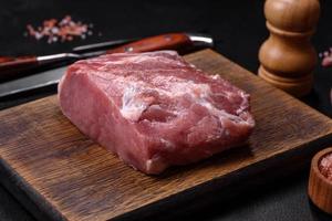 Fresh piece of raw pork with spices, salt and herbs on a wooden cutting board photo