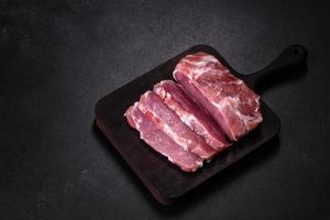 Fresh piece of raw pork with spices, salt and herbs on a wooden cutting board photo