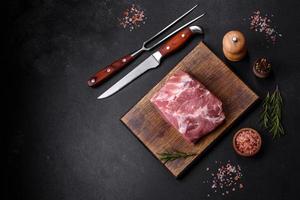 Fresh piece of raw pork with spices, salt and herbs on a wooden cutting board photo