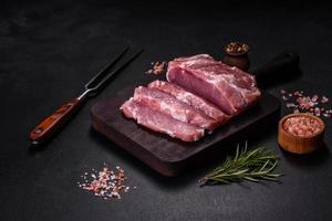 Fresh piece of raw pork with spices, salt and herbs on a wooden cutting board photo