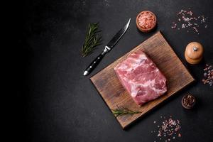 Fresh piece of raw pork with spices, salt and herbs on a wooden cutting board photo