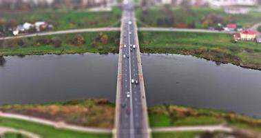 accelerated video with tilt shift effect on aerial view of road junction with heavy traffic on huge bridge over river