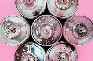 A few used spray cans with pink paint drips lie on texture background of fashion pastel pink color paper in minimal concept photo