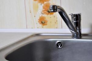 Empty clean silvery kitchen sink and water faucet close up photo