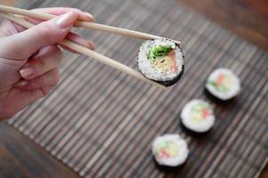 A hand with chopsticks holds a sushi roll on a bamboo straw serwing mat background. Traditional Asian food photo