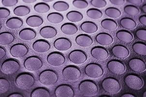 Black metal computer case panel mesh with holes on purple background. Abstract close up photo