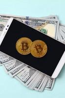 bitcoins se encuentra en un teléfono inteligente y billetes de cien dólares en un fondo azul claro foto