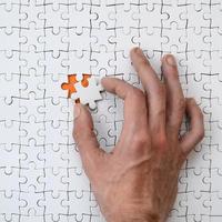 The texture of a white jigsaw puzzle in the assembled state with one missing element that the male hand puts in photo