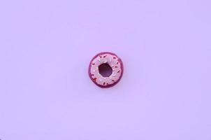 un solo donut de plástico pequeño se encuentra sobre un fondo de colores pastel. composición mínima plana. vista superior. foto
