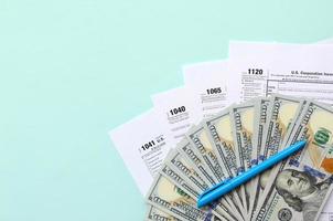 Tax forms lies near hundred dollar bills and blue pen on a light blue background. Income tax return photo