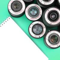 Several photographic lenses and white notebook lie on a bright turquoise background. Copy space photo