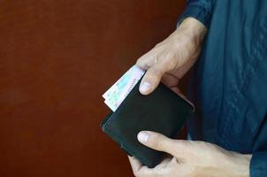 Man holds in hands black leather wallet with ukrainian money or thief who stole wallet full of money photo