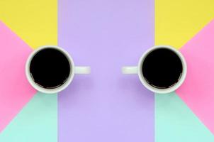 Two small white coffee cups on texture background of fashion pastel blue, yellow, violet and pink colors paper in minimal concept photo