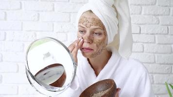 soins de beauté du visage. portrait d'une jeune femme séduisante mettant un gommage au café sur la peau du visage. femme appliquant un gommage pour le visage video