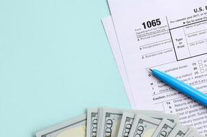 El formulario de impuestos 1065 se encuentra cerca de los billetes de cien dólares y el bolígrafo azul sobre un fondo azul claro. nosotros devolvemos los ingresos de paternidad foto