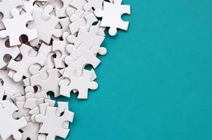 A pile of uncombed elements of a white jigsaw puzzle lies on the background of a blue surface. Texture photo with copy space for text