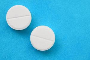 A few white tablets lie on a bright blue background surface. Background image on medical and pharmaceutical topics photo