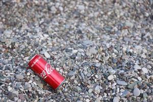 ANTALYA, TURKEY - MAY 18, 2022 Original Coca Cola red tin can lies on small round pebble stones close to sea shore. Coca-cola on turkish beach photo