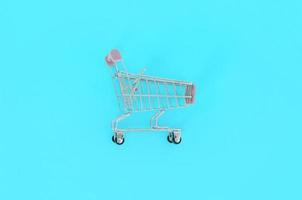 adicción a las compras, amante de las compras o concepto de adicto a las compras. un pequeño carrito de compras vacío se encuentra sobre un fondo de papel de color pastel. composición mínima plana, vista superior foto