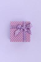 Small purple gift box with ribbon lies on a violet background. Minimalism flat lay top view photo